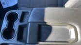 Center console of a car with two cup holders, a small storage tray, and a padded armrest beside a patterned car seat edge.