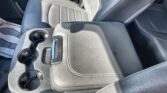 Interior of a car focusing on the center console with multiple cup holders and a black leather armrest/seat nearby.