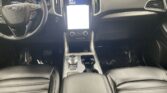 Interior of a modern car with a vertical touchscreen center display, steering wheel on the left, and black leather seats.