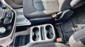 Front interior of a car showing the center console with cup holders and climate control panel beside a black fabric seat.