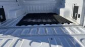 Empty white pickup truck bed with a black rubber mat, viewed from the tailgate.