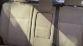 Rear passenger seats in a beige car; middle seat folded up as armrest with headrest, and visible seat belts.