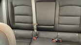 Back seat of a car in gray fabric with three seat belts and red buckles visible in the seats.