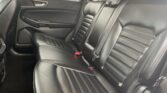 Rear passenger area of a car with black leather seats, visible stitching, and red buckle tips on the seat belts.