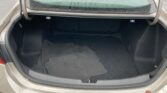 Open car trunk with black carpeting and folded floor mats inside; raindrops on the rear window and wet ground outside.