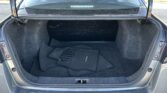 Open car trunk showing spacious cargo area with dark carpeting and stacked Versa floor mats; rear seats visible through rear window, slight dust.