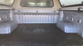 Empty pickup truck bed with ribbed metal walls, wheel wells, and rear window visible from the tailgate area