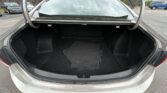 Open car trunk showing black interior and stacked floor mats in the cargo area, outdoor parking lot with other cars in the background
