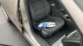 Front seat area of a car with the door open; black fabric seat, center console, and papers resting on the seat, raindrops on the window and door frame outside.