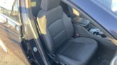 Interior of a dark car showing the front seat and center console through an open door, gray fabric upholstery and headrest visible in sunlight