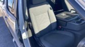 Interior of a vehicle showing the front seats and center console; driver’s door is open and the seat belts are visible in a black fabric interior.