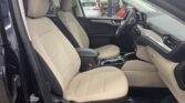 Front interior of a beige leather SUV, showing driver and passenger seats, center console, and steering wheel. In a workshop bay with another car in the background.