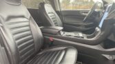 Car interior: front black leather seats, center console, and large vertical touchscreen in a modern SUV interior.