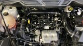 Under-hood view of a car engine with coolant reservoir on the left and various hoses and wires scattered throughout the bay.
