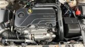 Under-hood view of a car engine with an ECOTEC cover, radiator, and battery nearby.