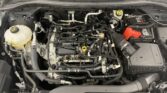 Open car hood showing the engine bay with a battery on the right, yellow-capped coolant reservoir on the left, and many hoses/wires.