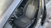 Interior of a car showing the driver's seat with dark fabric upholstery and white stitching, open door beside the seat.