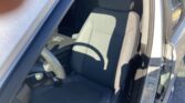 Front driver's seat area of a car with the door open, showing gray fabric upholstery and part of the steering wheel.