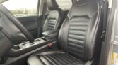 Front interior of a car showing black leather driver and passenger seats with white stitching and a center console with gear selector visible under the armrest.