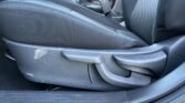 Close-up of a dark car interior: fabric seat with a visible seat belt buckle and a scuffed plastic panel near the door.