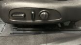 Close-up of a car seat side adjustment panel with a horizontal lever, a small vertical switch, and a round dial/button for seat adjustments.