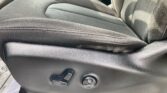 Close-up of a car driver's seat side with adjustment controls (two levers and a round dial) on black fabric upholstery with visible stitching