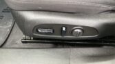 Close-up of a car seat adjustment panel with a lever, round knob, and sliding rail on a black fabric seat.