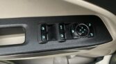 Close-up of a driver's door control panel with window switches and a circular mirror-control dial, on a textured black surface and beige trim, blue backlit icons near the buttons