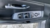 Interior of a car door panel featuring a silver door handle, black window and mirror control buttons, and carbon-fiber trim.