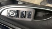 Close-up of a car door panel showing a circular mirror-adjustment knob and several window switches on the armrest