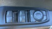 Close-up of car interior control panel showing window switches and a round multi-function joystick/dial on a black textured surface.