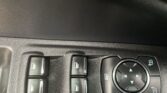 Close-up of car window switch panel with four window buttons and a round multi-directional control dial on a black textured dashboard edge