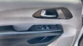 Interior car door panel: textured beige surface, silver handle, and window/mirror control buttons on the armrest with a speaker grille nearby.