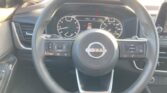 Close-up of a Nissan steering wheel from the driver’s seat, with the instrument cluster and center display in view.
