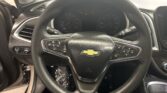 Close-up of a Chevrolet steering wheel inside a car, showing the instrument cluster behind it and cruise control buttons on the wheel.