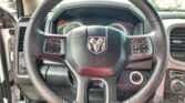 Steering wheel with Ram logo and mounted controls, dashboard gauges visible behind it in a car interior