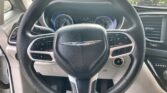 Close-up of a car steering wheel with Chrysler emblem, dashboard gauges, and gear selector visible from the driver’s seat perspective.