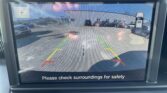 Rear camera display: parking lot with cars, green/yellow/red guide lines; safety message 'Please check surroundings for safety' at bottom.