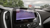 In-car viewing screen showing rear parking guide lines over a street scene as the car backs up in a parking lot.