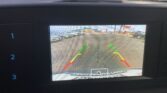 Rearview camera display: parking lot with cars on both sides and colored guiding lines (green, yellow, red) for distance.