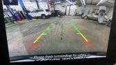 Rear-view camera display in a garage showing colored parking guide lines (green, yellow, red).
