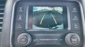 Car infotainment screen displaying the rear-view camera with colored guiding lines while parked, surrounded by control buttons for Radio, Media, Compass, Settings, and more.