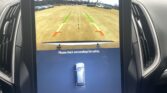 Rearview camera display with parking guide lines (green/yellow/red) showing the path behind the car and a safety warning: 'Please check surrounding for safety.'