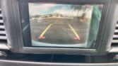 Car's rearview monitor displaying a parking area with yellow guiding lines and red end markers toward a building entrance.