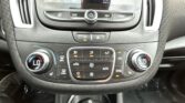 Close-up of a car's center console with touchscreen display, row of control buttons, and climate dials visible; Chevrolet key fobs at bottom edge.