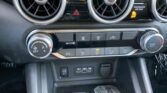 Car dashboard with two circular air vents, central hazard button, and climate control knobs visible on a black panel.