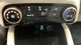Climate control panel in a car: left circular fan speed dial, center row of illuminated function buttons, right temperature dial with blue/red gradient.