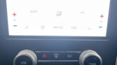 Close-up of a car's center console with a bright touchscreen showing phone, climate, and media icons, plus large volume and tune knobs.