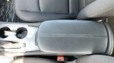 Center console of a car's front interior with two cup holders, gear shifter, and black leather seats/armrest nearby